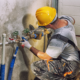 Plumber in a yellow hard hat repairs a water pipe with a wrench.